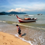 A kid at the water&#039;s edge on the beach at Batu Ferringhi, Penang